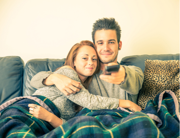 Happy couple watching television on the couch with blanket